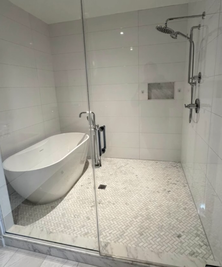 Freestanding tub beside a glass shower with herringbone tile floor