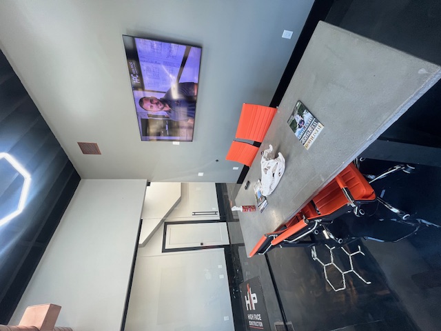 Office meeting table with orange chairs and a wall-mounted screen